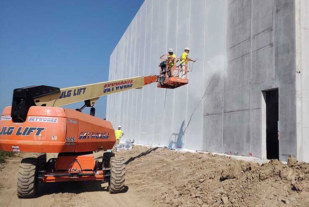 Workers on lift spraying paint on exterior of commercial property